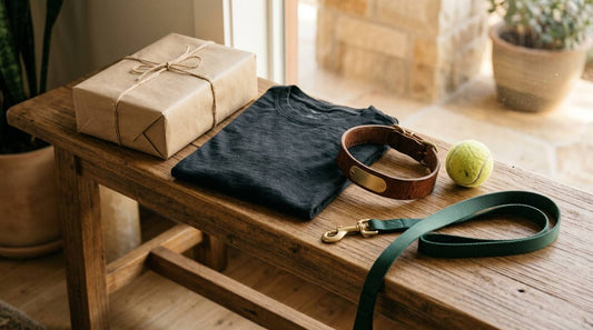 Wrapped gift, folded dark shirt, dog collar, leash, and tennis ball on a wooden bench